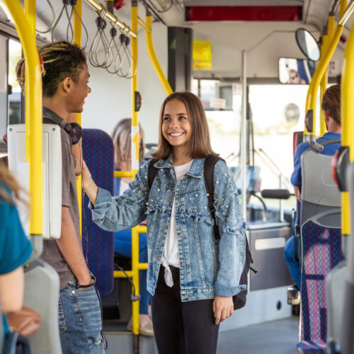 Ein Junge und ein lächelndes Mädchen stehen im Bus und sprechen miteinander.
